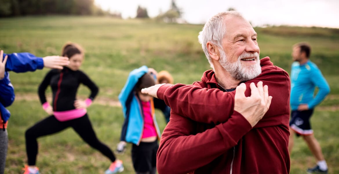 A large group of fit and active people doing exercise in nature, stretching.